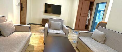 A living room with a sofa, armchairs, a coffee table, and a flat-screen TV mounted on the wall.
