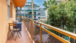 A balcony with a table and chair, overlooking a residential area with multiple buildings and a tree. - Costa Brava by Interhome (Salou)