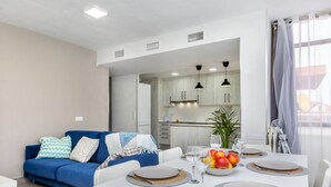 A modern living room with a blue sofa, a dining table set for four with placemats, and a kitchen in the background. - Costa Brava by Interhome (Salou)