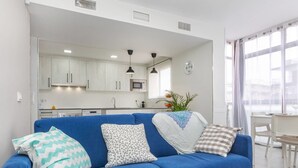 A modern living room with a blue sofa, a kitchen in the background, and a dining area with a table and chairs. - Costa Brava by Interhome (Salou)