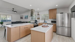Une cuisine moderne dotée d’un îlot central, d’appareils électroménagers en acier inoxydable, d’armoires en bois et d’un ventilateur de plafond.