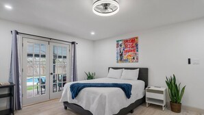 Une chambre à coucher avec un lit, une table de chevet, une plante en pot et une vue sur l’extérieur, visible à travers une porte vitrée.