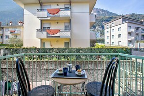 A balcony with a table set for two, featuring a coffee pot, cups, and a plate with food.