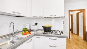 Ett modernt kök med vita skåp, en diskho i rostfritt stål, en gasspis och ett urval av färska grönsaker och frukter på bänkskivan.