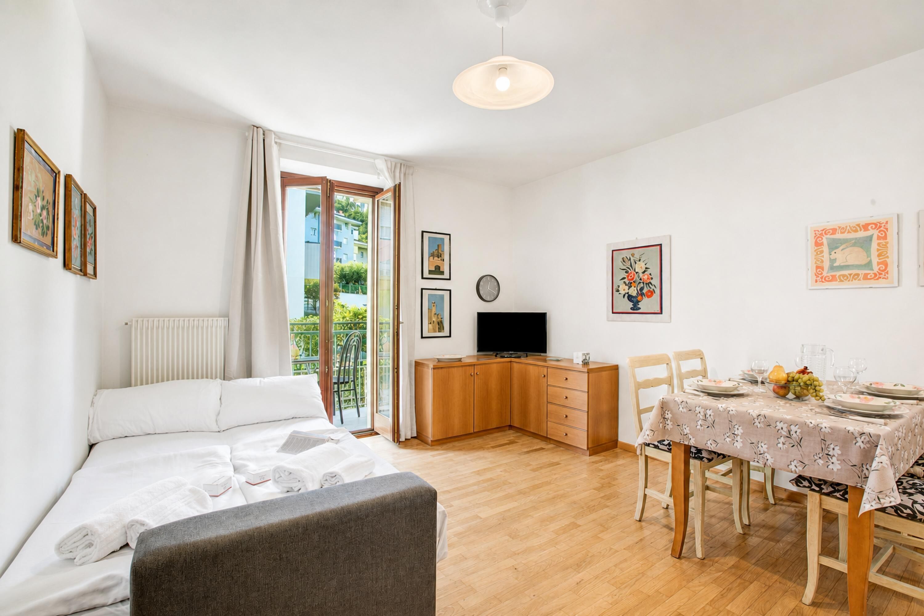 A hotel room with a bed, a desk, a dining table set for two, and a TV.