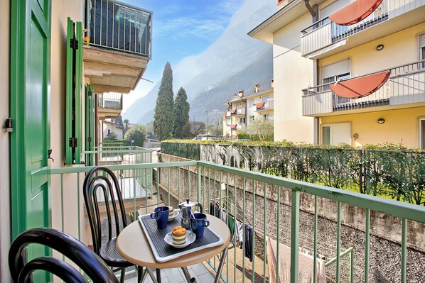 A balcony with a table set for two, overlooking a street with buildings and a mountain in the background.