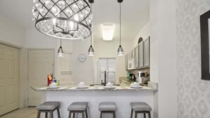 A kitchen with a central island, bar stools, pendant lights, and a patterned wall.