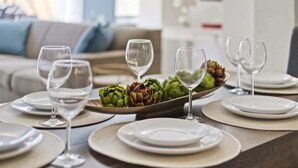 A dining table set with plates, glasses, and a wooden board with artichokes.