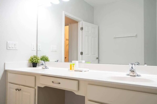 A bathroom with a white sink, two faucets, a mirror, and a door leading to another room.