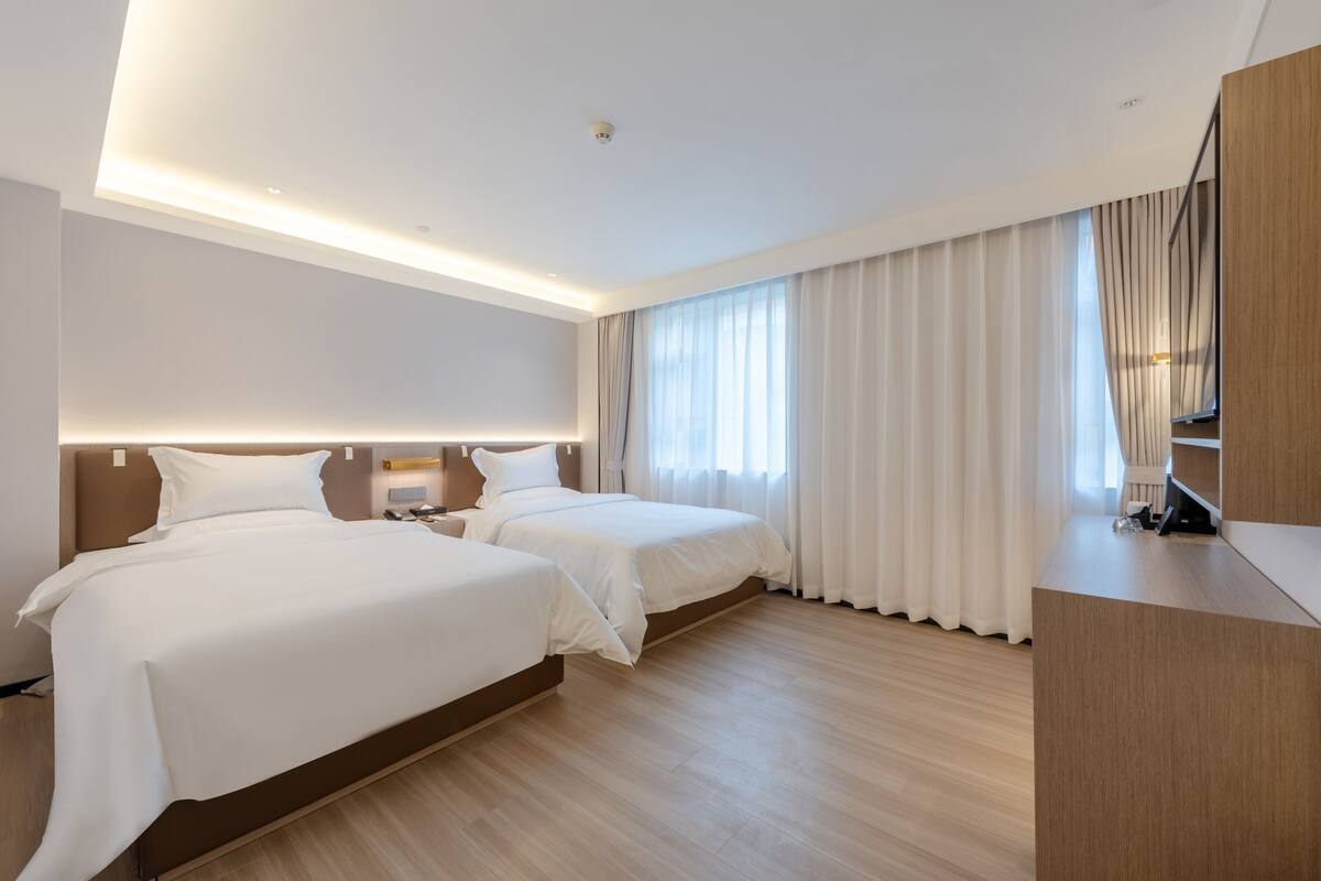 A modern hotel room with two beds, a desk, and a large window with curtains.