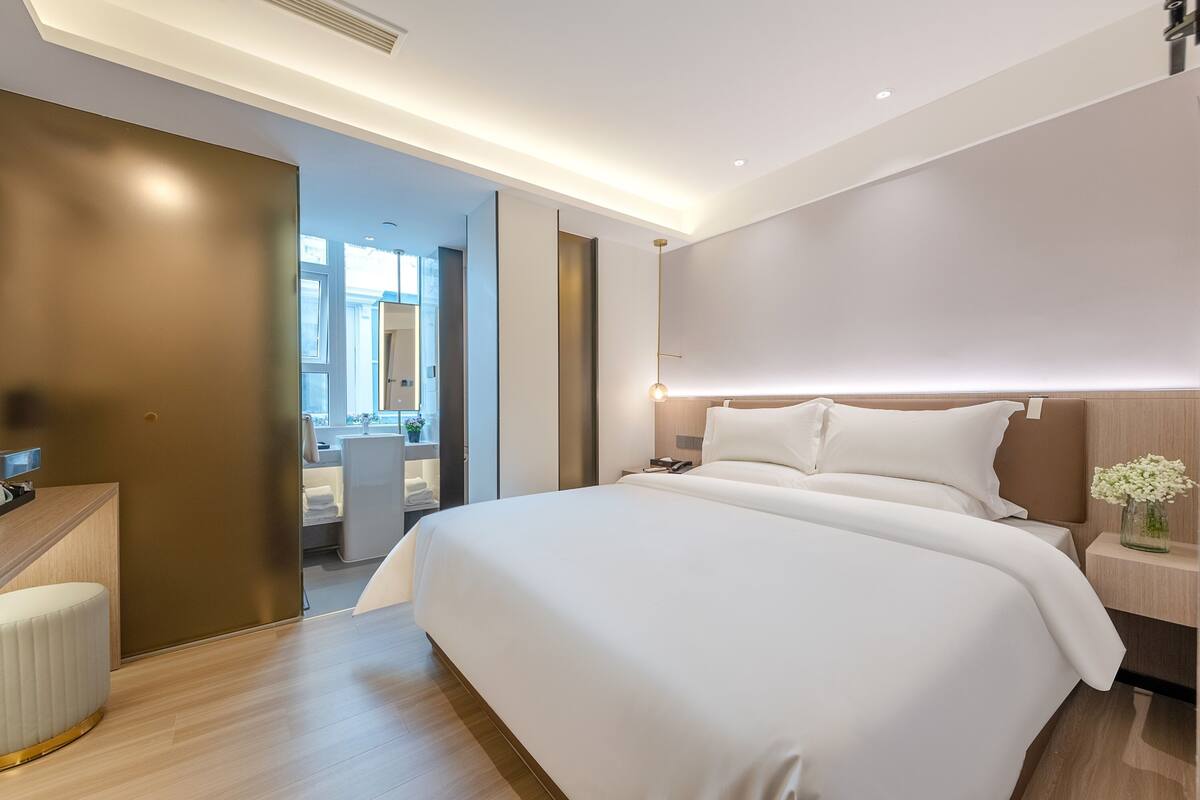 A modern hotel room with a large bed, a desk, and a bathroom visible through an open door.