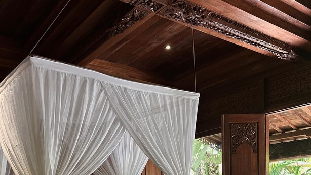 A bed with a canopy, wooden headboard, and a nightstand with a lamp. - Darta Ubud Joglo Villa by EPS (Ubud)