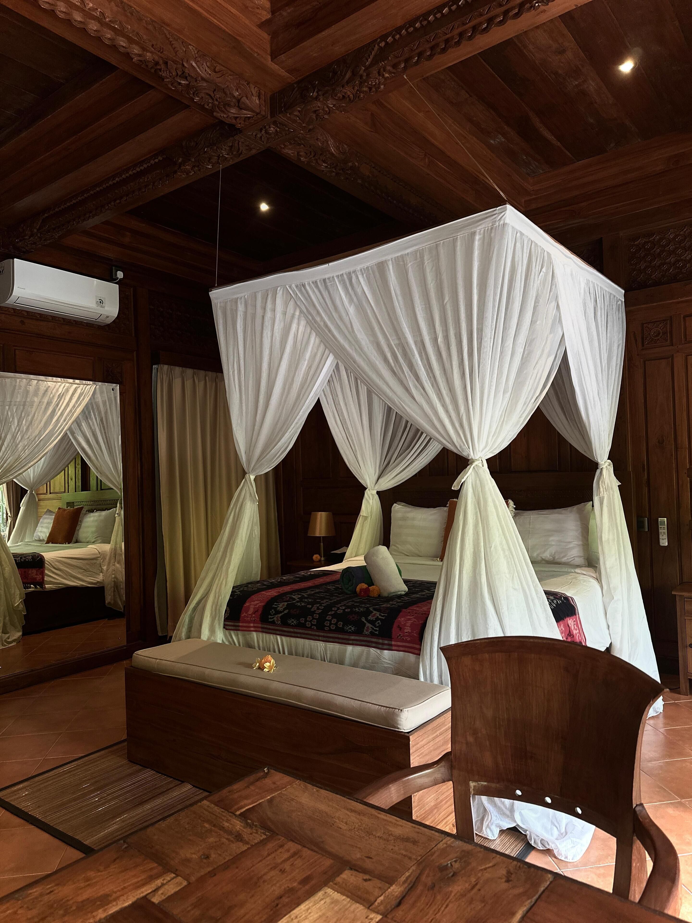 A four-poster canopy bed with a headboard, a bedside table, and a chair.