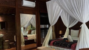 Een slaapkamer met houten vloer, een bed onder een hemelbed en een bakstenen muur.