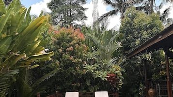 Un área de piscina con dos sillones de descanso y una pequeña mesa, rodeada de exuberante vegetación tropical y palmeras.