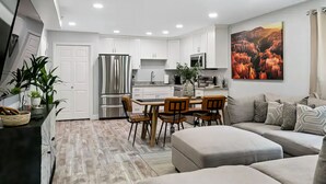 Una cocina moderna con armarios blancos, un refrigerador de acero inoxidable y una zona de comedor con sillas de madera.