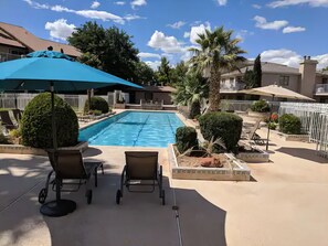 A swimming pool with lounge chairs and umbrellas, surrounded by greenery and fences.