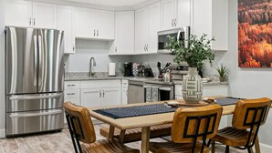 Una cocina moderna con armarios blancos, electrodomésticos de acero inoxidable y un comedor con mesa de madera y sillas de cuero.