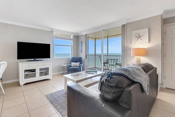 A living room with a TV, sofa, and balcony with a view.