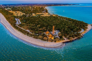 An aerial view of a coastal area with a lighthouse, clear blue waters, and a sandy beach.
