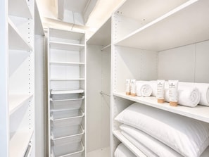 A white storage unit with shelves and a hanging rack, containing rolled towels and toiletry items.
