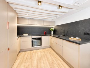 A modern kitchen with a black countertop, stainless steel appliances, and a wooden floor.