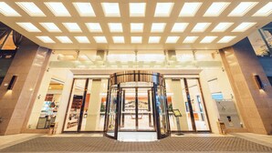 Una entrada de hotel con puerta giratoria, grandes ventanales y suelo de baldosas.