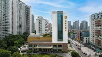 A modern hotel with a prominent vertical glass facade, surrounded by high-rise residential buildings and a busy street.