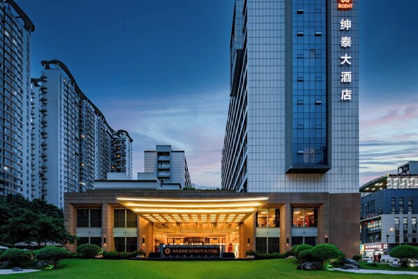 A hotel with a modern facade, a well-lit entrance, and a sign indicating it is a Grand Scent Hotel.