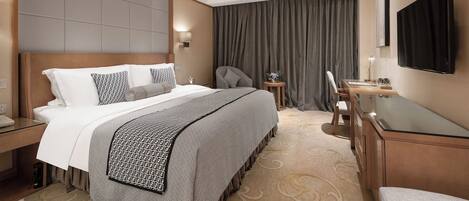 A hotel room with a large bed, a desk with a chair, a TV, and a small table with a lamp.