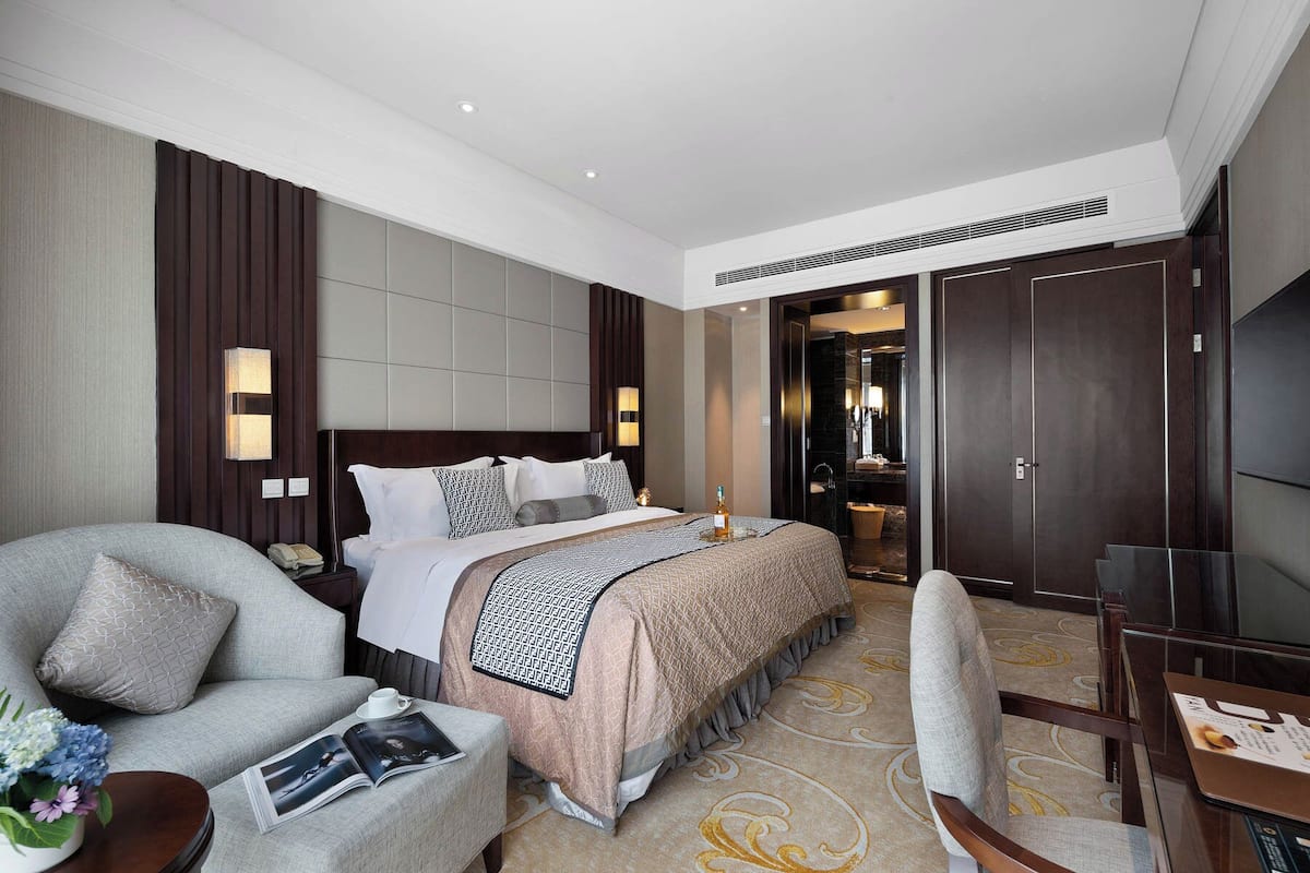 A hotel room with a bed, a sofa, a desk, and a bathroom visible through an open door.