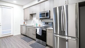 A modern kitchen with stainless steel appliances, light wood cabinets, and a grey tiled backsplash. - The Library - Comfy Studio Gym & Pet Friendly (Dallas)