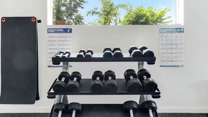 A gym with a dumbbell rack, a stretching exercise chart, and a window with a view of trees. - The Library - Comfy Studio Gym & Pet Friendly (Dallas)