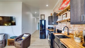 A modern kitchen with a brick wall, wooden cabinets, and a stainless steel refrigerator. - Walk to Shops & Eats: Charming Dtwn Emmett Apt! (Emmett)