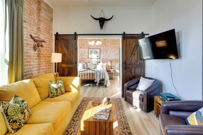 A living room with a yellow sofa, a brown leather couch, a wooden coffee table, and a TV mounted on the wall. - Walk to Shops & Eats: Charming Dtwn Emmett Apt! (Emmett)