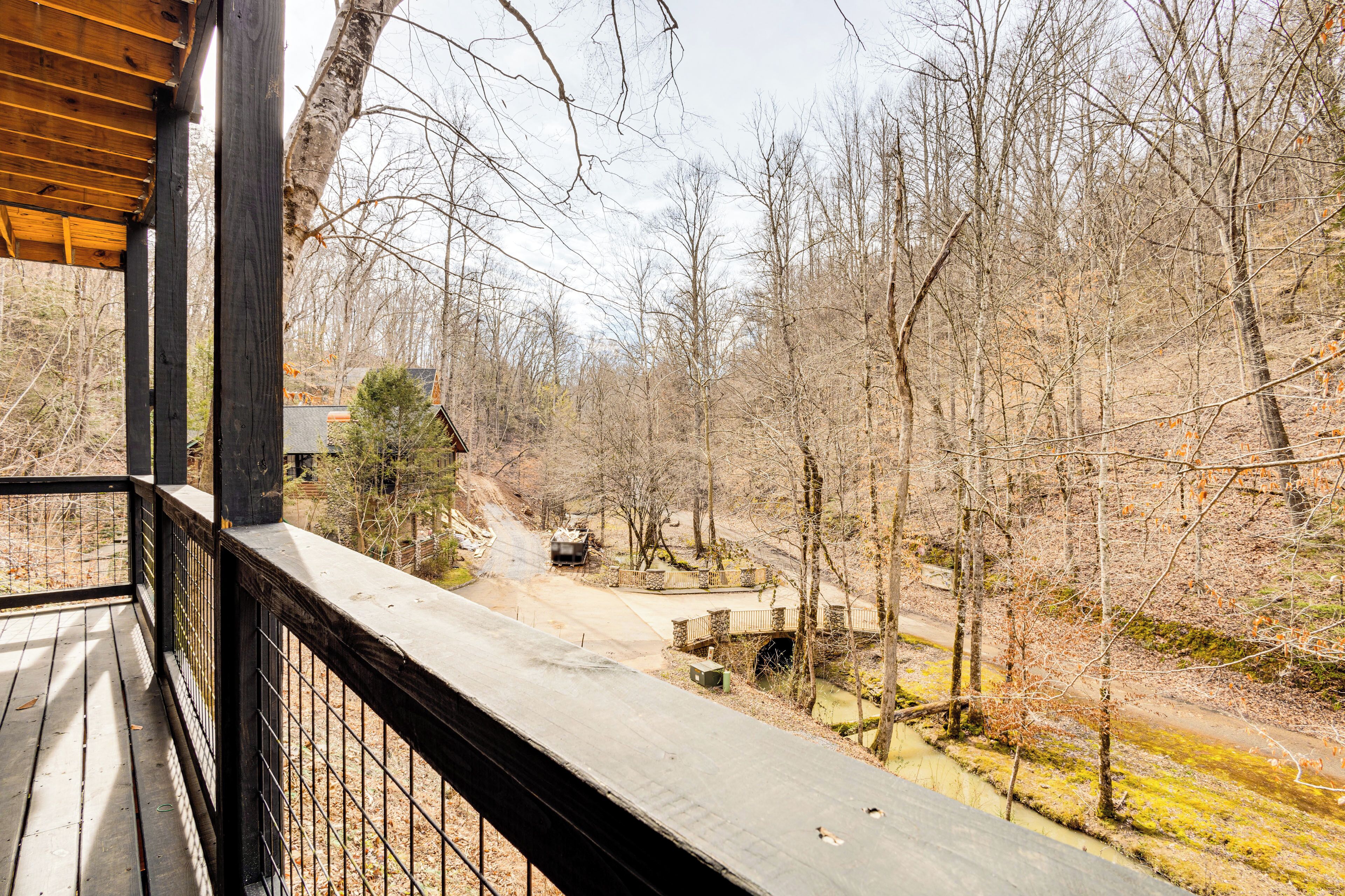 A wooden deck with a view of a forested area, a stone bridge, and a dirt path.