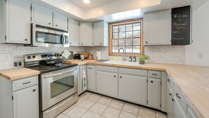 A modern kitchen with stainless steel appliances, white cabinetry, and a chalkboard sign indicating Wi-Fi access. - Deck & Fire Pit: Cozy Escape in Morrisville! (Morrisville)