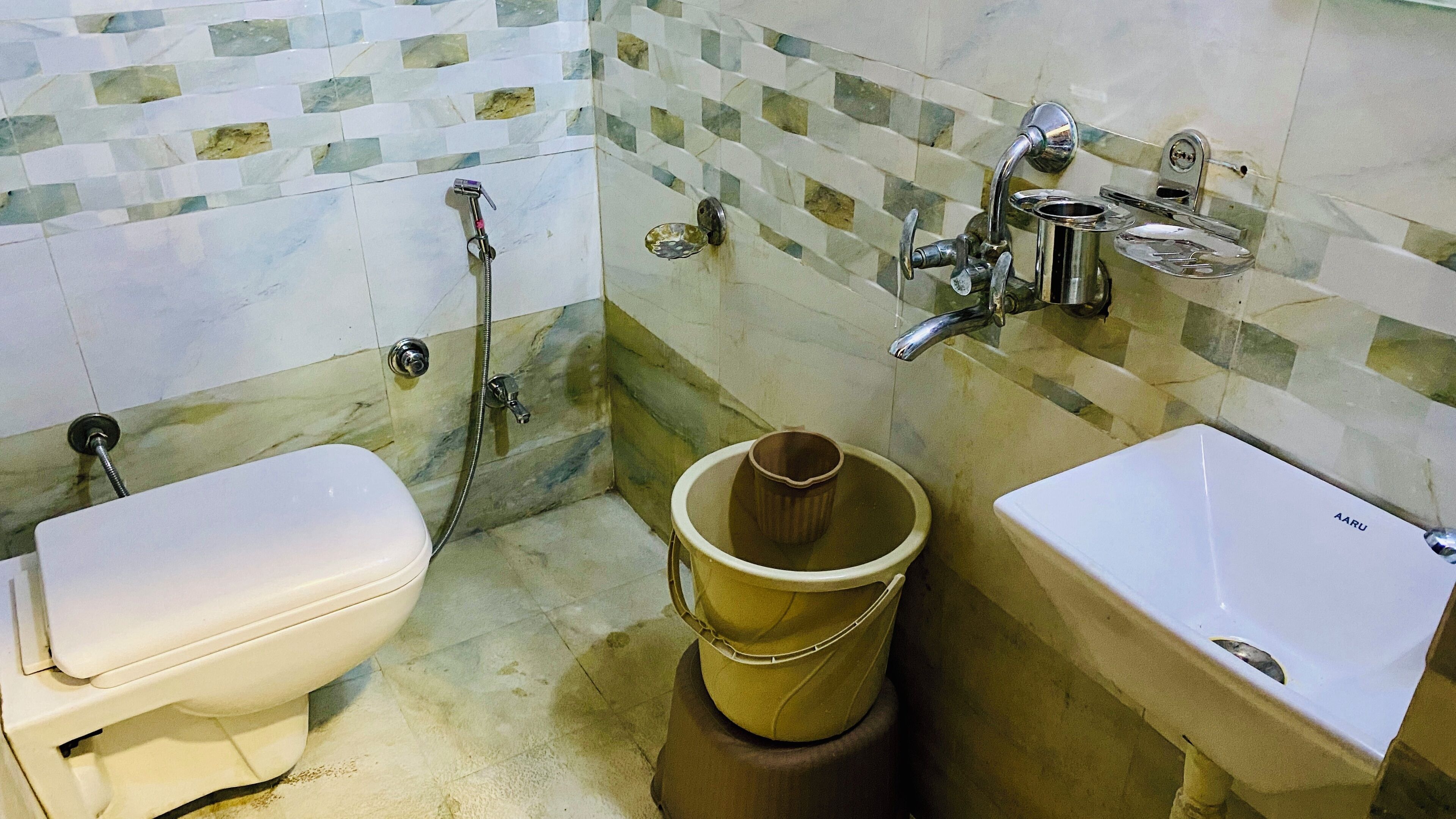 A bathroom with a toilet, a bucket, and a sink.