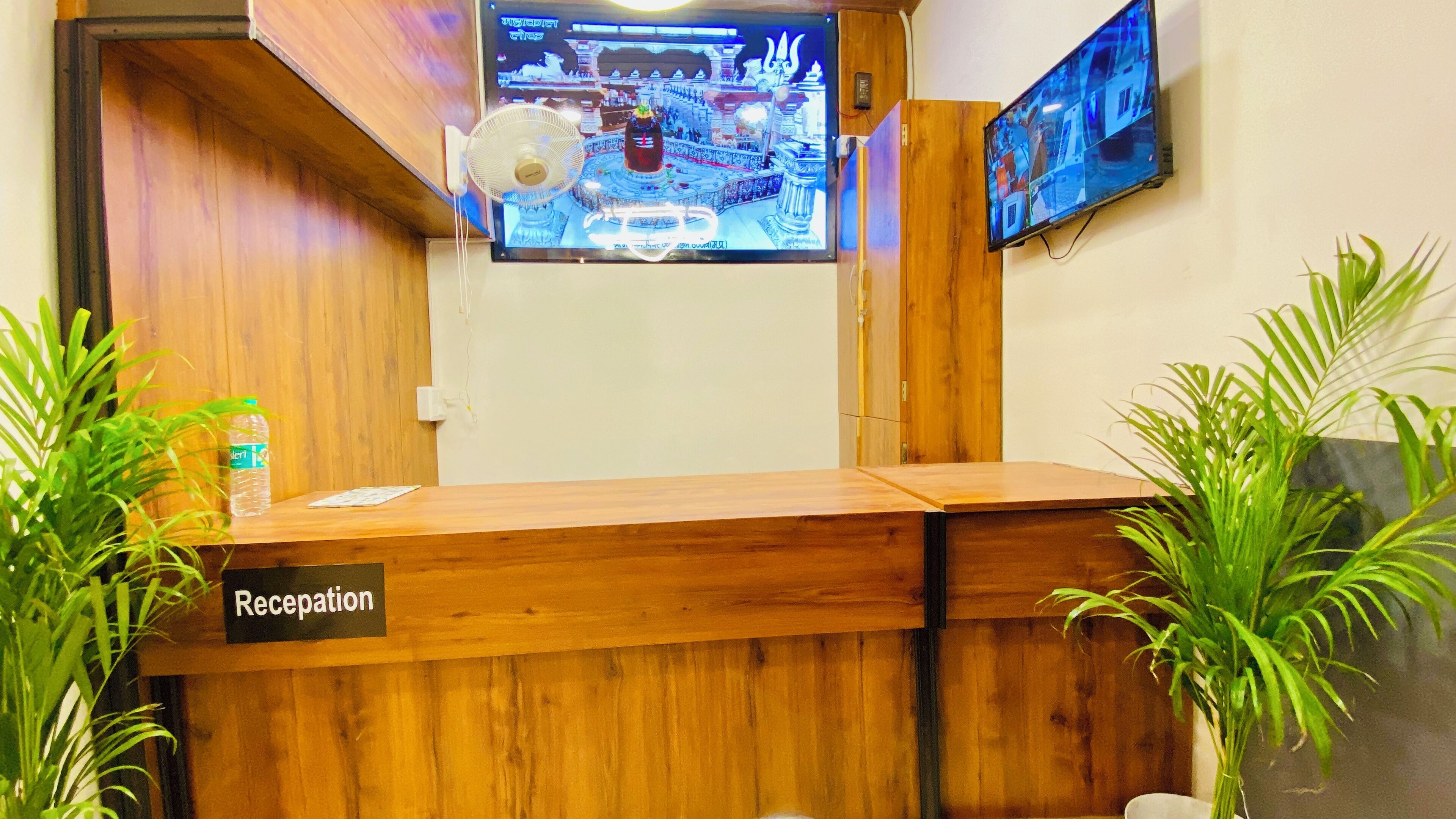 A reception desk with a sign, a television mounted on the wall, and a fan above it.
