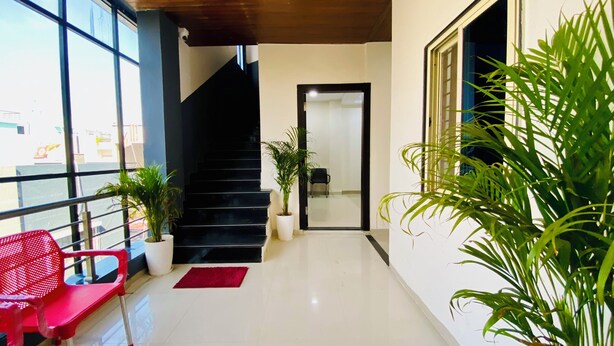 Un pasillo limpio y moderno con una escalera, plantas en macetas y una silla roja.