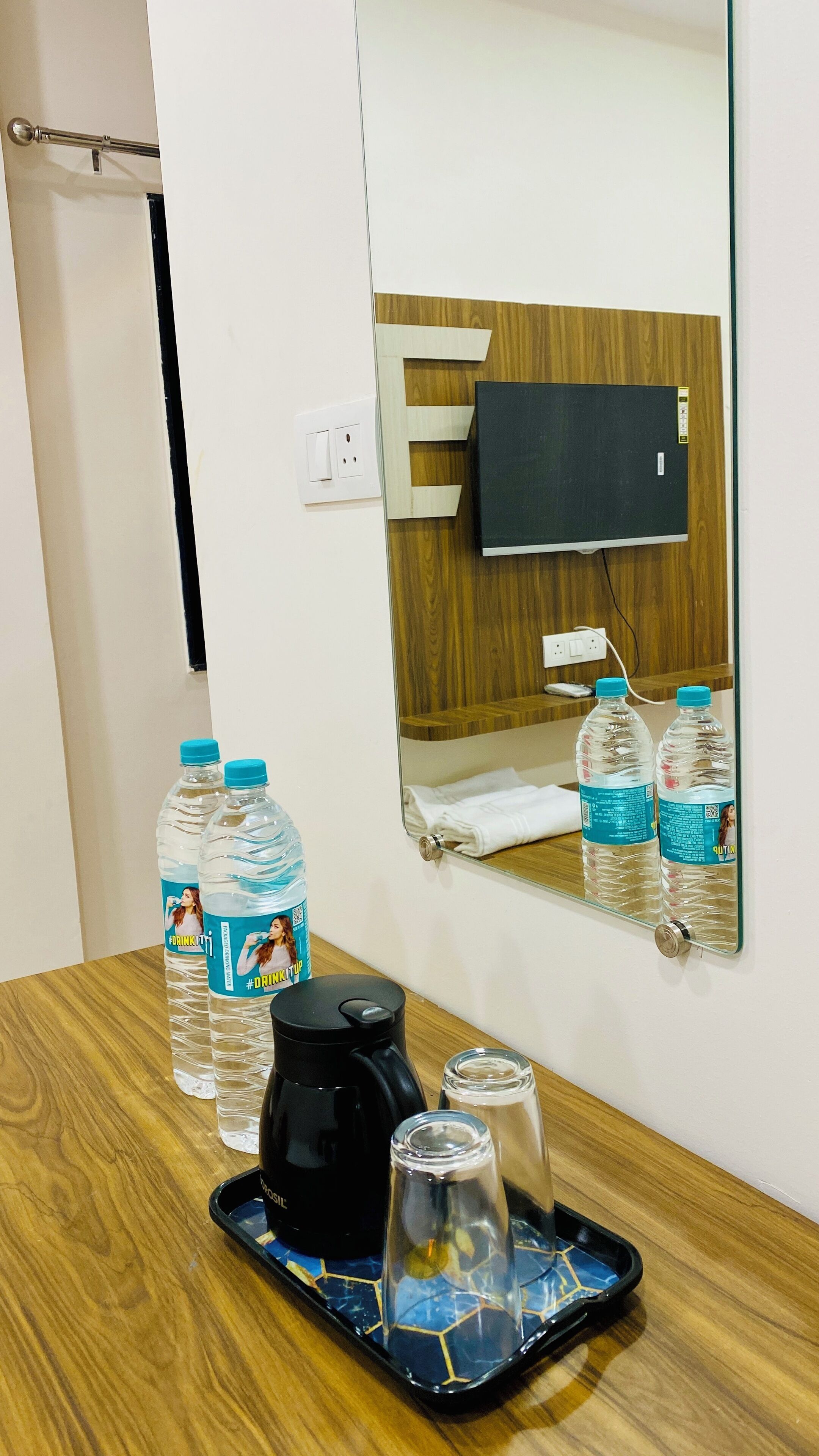 A hotel room with a wooden table, two water bottles, a coffee maker, a glass, and a tray.