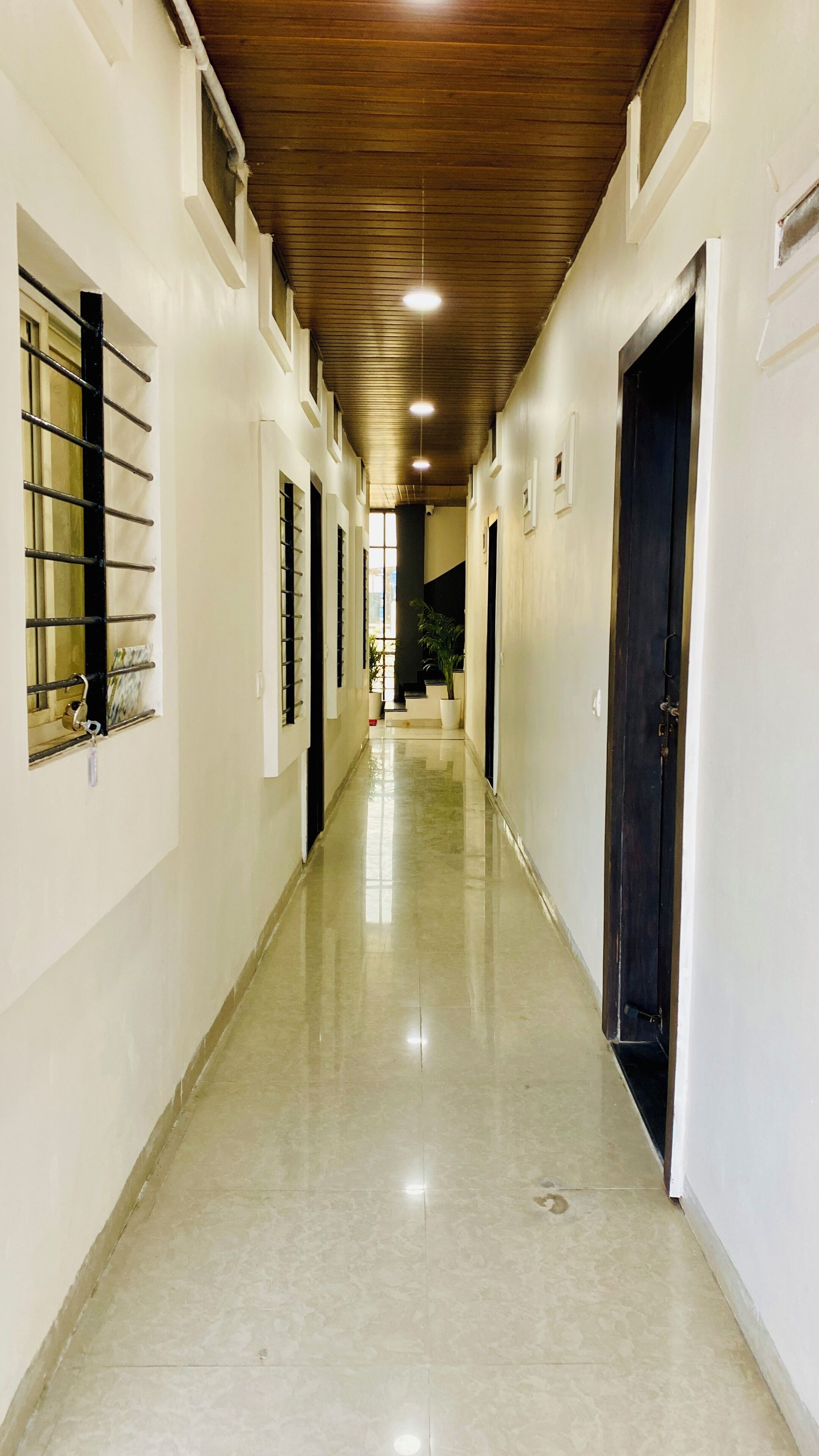 A long, narrow hallway with a polished floor, white walls, and a wooden ceiling.