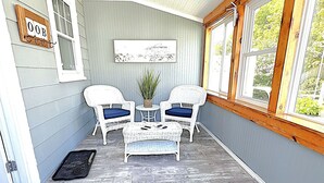 Une véranda avec deux fauteuils en osier, une petite table et une plante en pot.