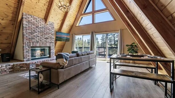 A spacious loft with a brick fireplace, a large sofa, and a dining table. - Charming A-Frame home,  wood fireplace,  7 miles to The Village and ski resorts. (Sugarloaf)