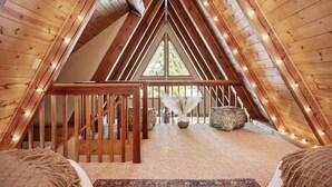 A cozy attic bedroom with wooden beams, a wooden staircase, and a large window. - Charming A-Frame home,  wood fireplace,  7 miles to The Village and ski resorts. (Sugarloaf)