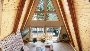 A spacious loft with a sloped ceiling, a brick fireplace, a large sofa, and a dining area. - Charming A-Frame home,  wood fireplace,  7 miles to The Village and ski resorts. (Sugarloaf)