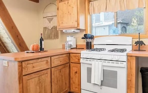A kitchen with wooden cabinets, a white stove, and a window with a view of a house. - Charming A-Frame home, wood fireplace, 7 miles to The Village and ski resorts. (Sugarloaf)