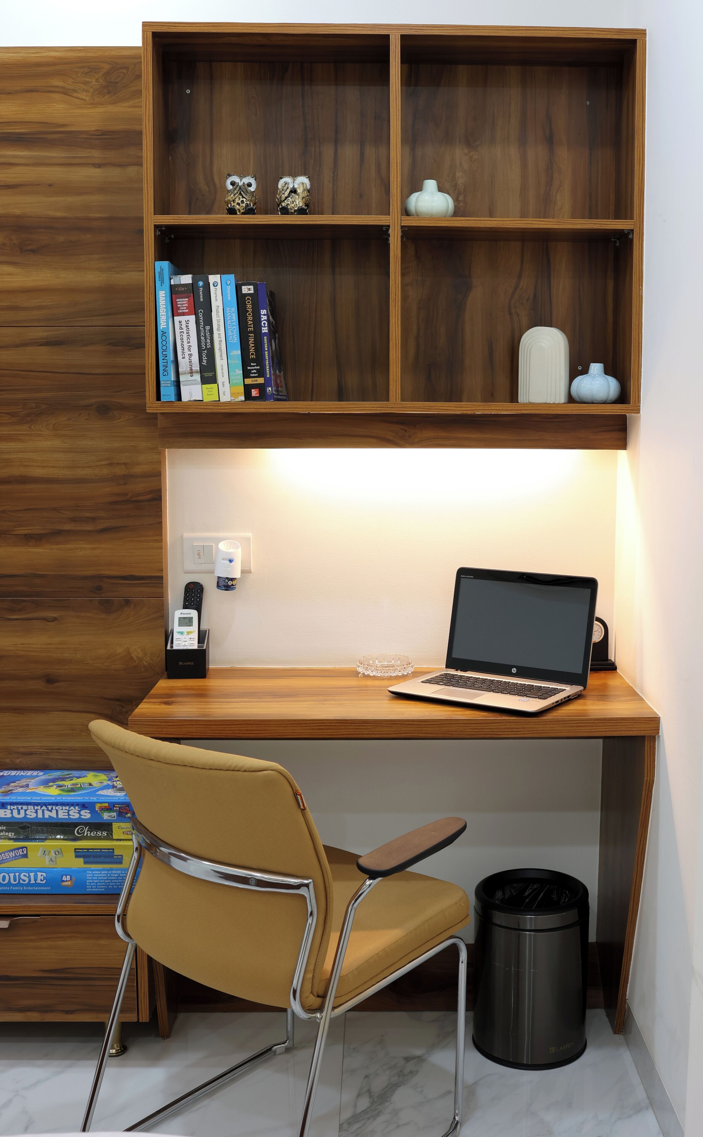Un espacio de trabajo con un escritorio de madera, una computadora portátil, una silla, una estantería y un cubo de basura.