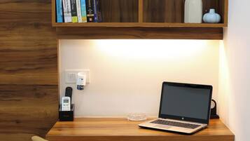 A workspace with a wooden desk, a laptop, a chair, a bookshelf, and a trash can.