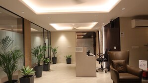 Un área de recepción moderna con mostrador, asientos y plantas en macetas.